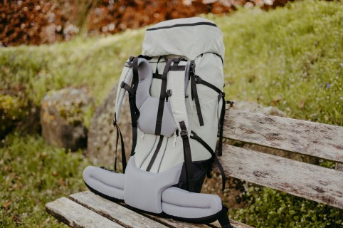 Ein großer, grauer Trekkingrucksack steht auf einer Holzbank im Grünen.