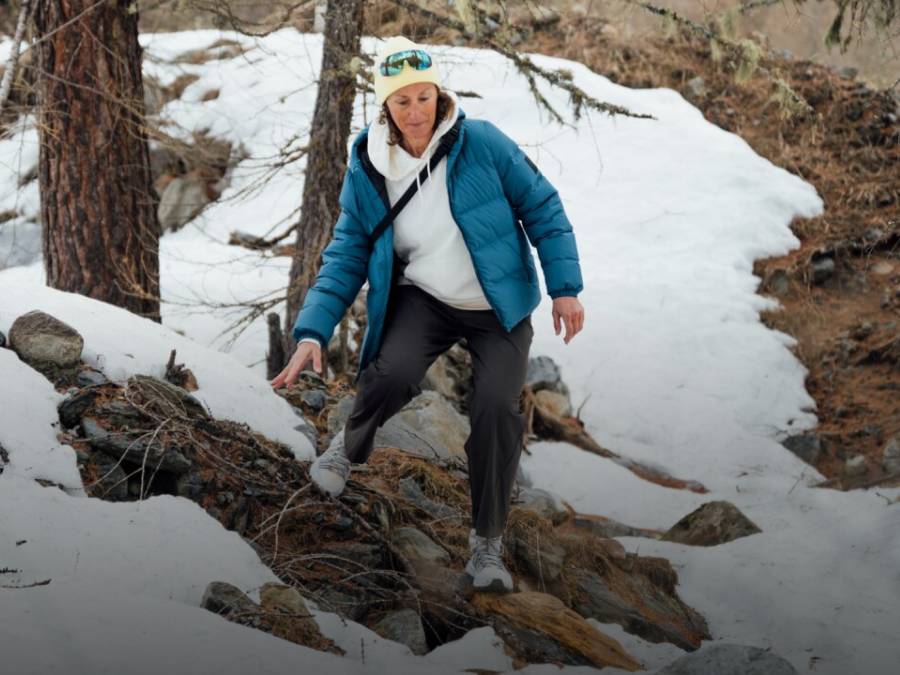 Zwei Schlitten mit je zwei Personen fahren eine verschneite Piste hinunter. Die Personen lachen und tragen Winterkleidung, Mützen und Sonnenbrillen; im Hintergrund schneebedeckte&nbsp;Berge.