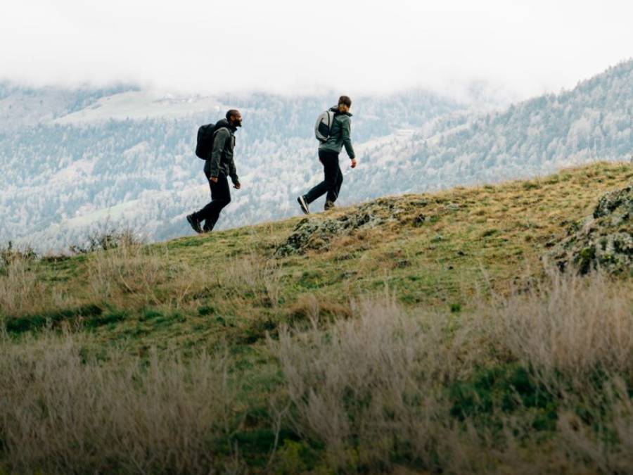 Zwei Personen in hebstlicher Wanderbekleidung wandern über einen Berg