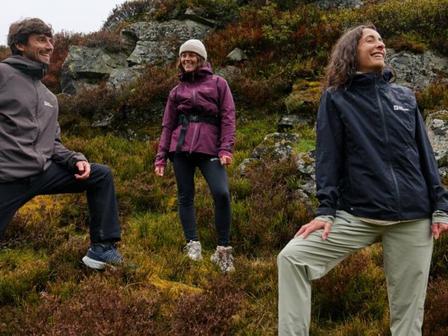 Drei Freunde stehen lächelnd auf einem bergigen Terrain und blicken in die Landschaft