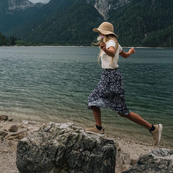Frau in sommerlicher Outdoor-Kleidung balanciert auf Steinen an einem See