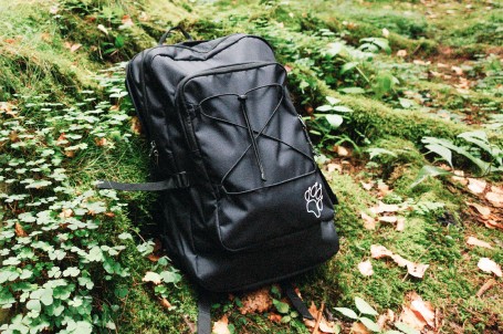 Mann mit Rucksack wandert in einem grünen, bergigen Gebiet.