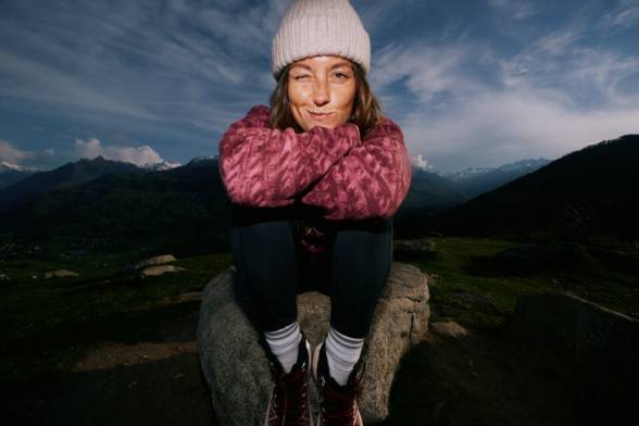 Junge Frau in sportlicher Wanderbekleidung hockt auf einem Felsen in der Dunkelheit