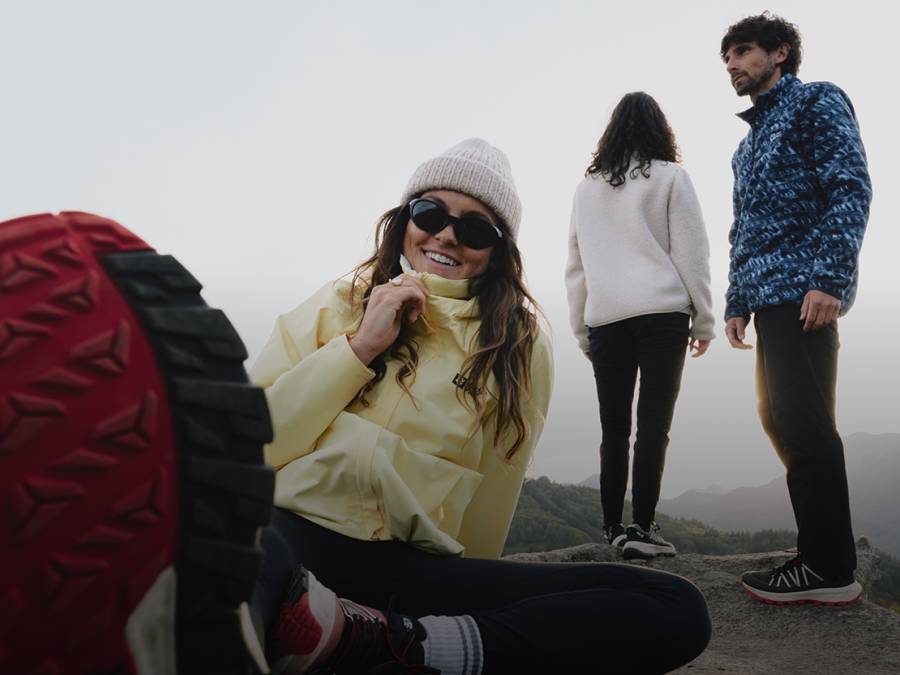 Drei junge Erwachsene in sportlicher Outdoorbekleidung halten sich in einer bergigen Landschaft auf
