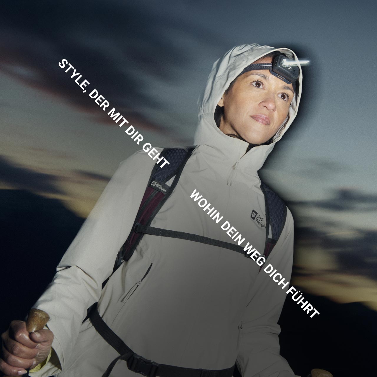 Eine Person in Outdoor-Ausrüstung mit einer Stirnlampe blickt nach vorne und hält Trekkingstöcke in der Bergdämmerung. Der Text lautet: „Style, der mit dir geht wohin dein Weg dich führt“